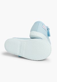 Zapatilla de lona azul claro con suela de goma blanca, que presenta una correa de Velcro y una suela texturizada. Incluye la marca en el talón.