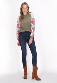 Oliven grøn ribbet sweatshirt med blomster, mønstrede lange ærmer; parret med mørkeblå skinny jeans og brune ruskinds ankelstøvler.