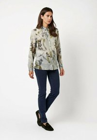 Floral button-up shirt in light green and gray, with long sleeves and a collar. Paired with dark blue jeans and dark slip-on shoes.