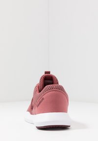 Růžová sportovní obuv s texturovaným síťovaným svrškem a hladkými doplňky. Má polstrovanou podešev a poutko na patě. Viditelné logo značky.