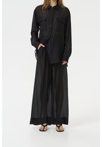 Chemise noire en voile, oversized, avec deux poches à l'avant, fermeture à boutons, et pantalon noir à jambes larges ; texture douce, design superposé.