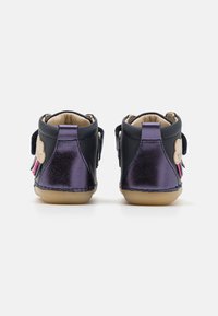 Chaussures en cuir avec un dessus bleu foncé, des accents métalliques violets et des semelles beiges. Dotées de sangles Velcro et d'un détail de pompon rose décoratif.