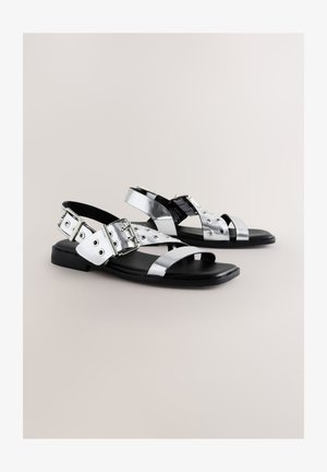 Ezüst metál lapos szandálok több pánttal és csatos díszítéssel, fekete talppal és sima textúrával.