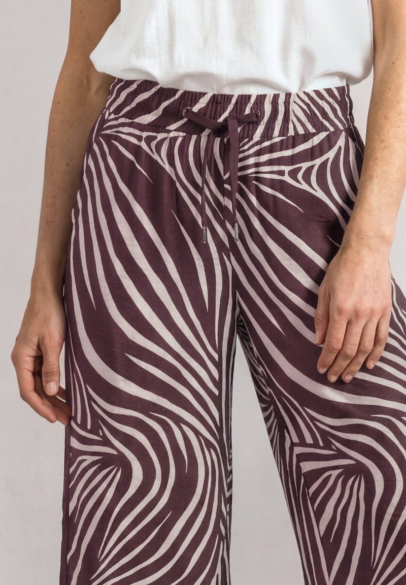 Gros plan d'une personne portant un pantalon à rayures zèbre violet et blanc avec une taille à cordon et un haut blanc rentré.