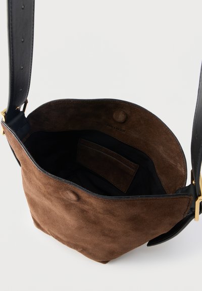 Brun ruskinds bucket-taske med sort justerbar læderrem og magnetisk tryklås, der viser en indvendig lomme og blød foring.