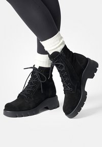 Bottines en daim noir avec une semelle en caoutchouc épaisse, design à lacets et fermeture éclair sur le côté. Comprend des chaussettes montantes côtelées de couleur crème.