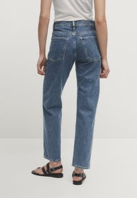 Högmidjade, raka blå denimjeans med två bakfickor och en ljus tvätt. Nådda med svarta platta sandaler.