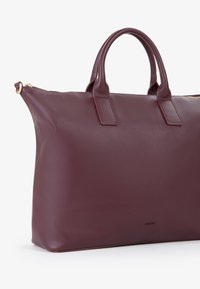 Borsa in pelle bordeaux con design strutturato, due manici corti, chiusura zip e superficie testurizzata. Accentuata da hardware dorato.