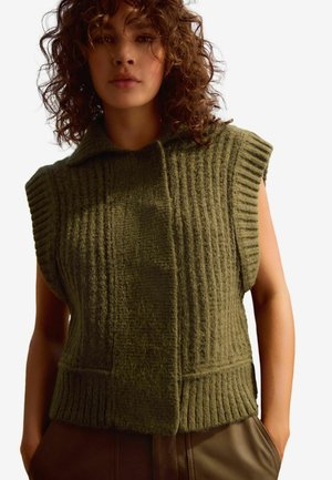 Gilet en tricot sans manches couleur kaki avec col montant, présentant une texture en côtes verticales et deux poches avant, réalisé en matériau doux et épais.