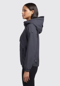 Veste à capuche gris foncé avec des poignets élastiques, des côtés zippés et un écusson logo sur la manche. Tissu lisse et design décontracté.