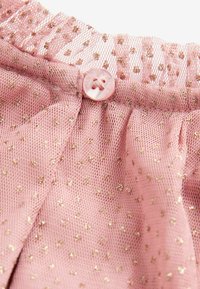 Tissu en tulle rose avec des pois dorés, froncé à une couture avec un petit bouton rond rose cousu dessus.