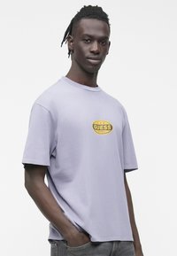 Lilijas rozā kokvilnas T-krekls ar apaļu kaklu un īsām piedurknēm. Centram izšūta dzeltena “GUESS” logo ar zvaigznītēm. Mīksta tekstūra un ērtas piegriezums.