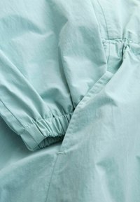 Tela azul claro texturizada con puño de manga fruncido. Presenta costuras limpias y una superficie lisa. Ideal para ropa de exterior.