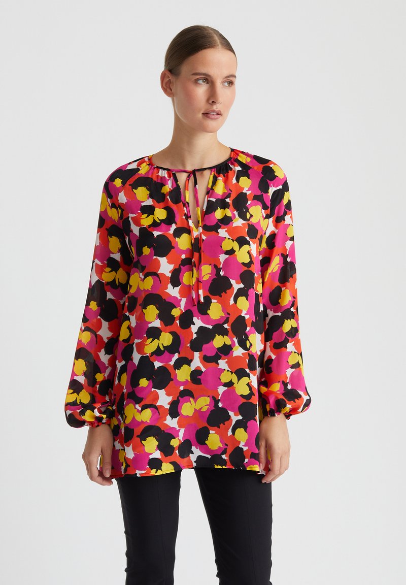 Langärmlige Bluse aus transparenter, floral gemusterter Stoff in den Farben Rosa, Gelb und Schwarz. Verfügt über einen Schlüssel-Ausschnitt mit einer Bindeschleife.