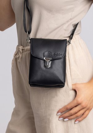 Black leather crossbody bag with a flap closure, metal clasp, and adjustable strap, featuring a smooth texture and embossed logo detail.