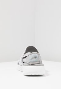 Scarpa slip-on Skechers grigia e bianca con tacco aperto e suola bianca imbottita, vista dal retro su una superficie bianca.