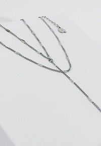 Srebrny naszyjnik z łańcuszka z wieloma pasmami i płaskimi, wydłużonymi ogniwami. Posiada mały, ozdobny wisiorek oraz zapięcie.