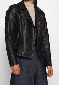 Giacca da motociclista in pelle nera con cerniera asimmetrica, colletto a risvolto e due tasche laterali con zip. Texture liscia, design aderente e hardware minimale.