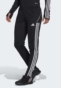 Zwarte sportbroek met witte strepen aan de zijkanten, voorzien van een elastische tailleband en een tapered leg ontwerp.