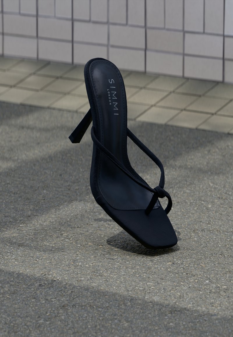 Μαύρο πέδιλο με ψηλό τακούνι, λεπτές λουρίδες και τετράγωνη μύτη, με τη μάρκα "SIMMI London", τοποθετημένο σε εξωτερικό πεζοδρόμιο κοντά σε πλακωμένο τοίχο.
