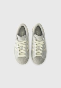 Szare i kremowe sneakersy Adidas z trzema białymi paskami, okrągłym noskiem, teksturowanym, gumowym czubkiem oraz sznurówkami w pasującym kolorze.