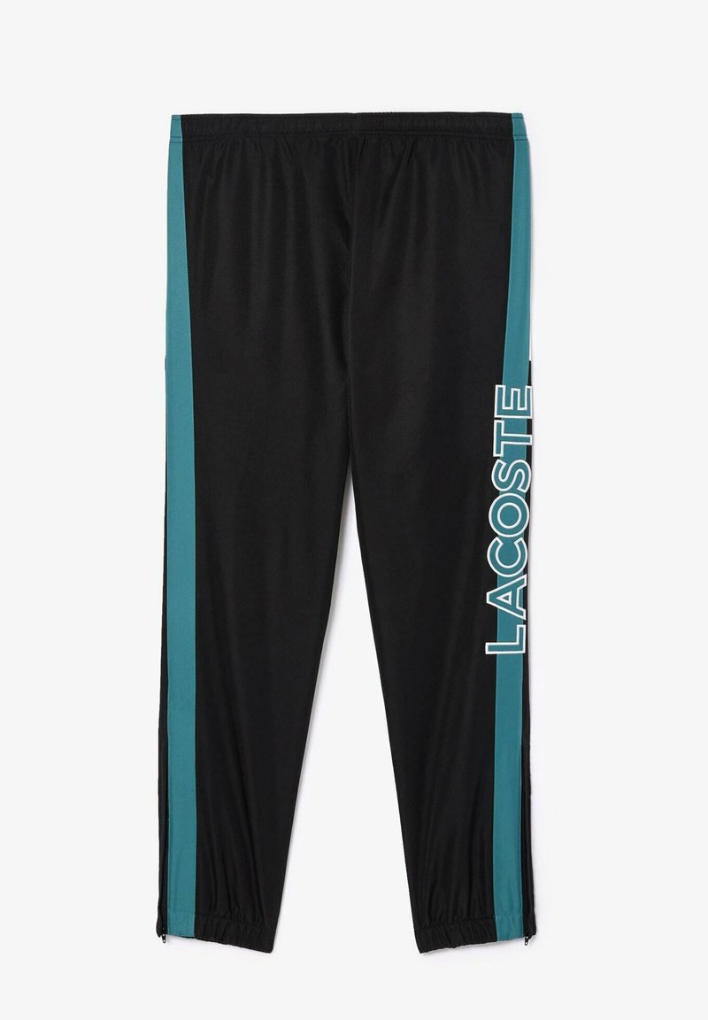Pantalons de survêtement noirs avec des rayures latérales teal et "LACOSTE" imprimé verticalement sur la jambe droite, dotés de poignets et d'une taille élastiques.