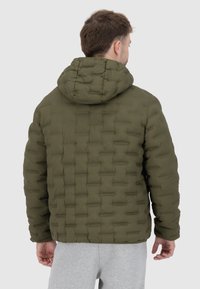 Olijfgroene pufferjack met een gewatteerd patroon, capuchon en elastische manchetten. Gemaakt van lichtgewicht materiaal met een gladde textuur.