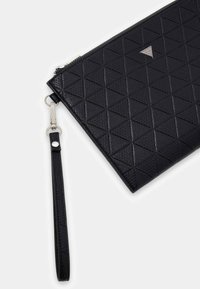 Czarna kopertówka z teksturowanym wzorem trójkątnym, zamknięciem na zamek błyskawiczny, odpinanym paskiem na nadgarstek oraz srebrnym logo.