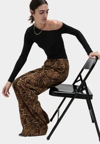Svart off-shoulder långärmad topp i kombination med bruna leopardmönstrade vida byxor. Sitter på en svart hopfällbar stol. Guldig kedja synlig.