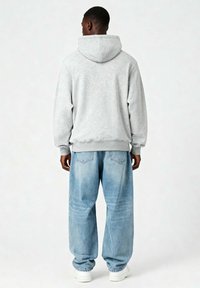 Felpa grigia con cappuccio e vestibilità rilassata, abbinata a jeans baggy blu chiaro. Sneakers bianche completano l'outfit. Tessuto morbido.