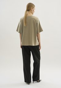 Camiseta de algodón de color verde oliva, de corte oversized y mangas cortas, combinada con pantalones negros de pierna ancha y zapatos de tacón negros. Diseño simple y textura suave.