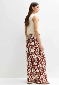Pantalons larges à imprimé floral avec fond rouille, présentant des fleurs et des feuilles blanches, ceinture élastique et tissu léger.