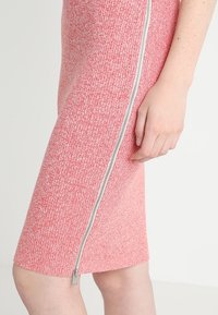 Abito rosa texturizzato fino al ginocchio con zip laterale. Il tessuto presenta un motivo sottile e una silhouette aderente.