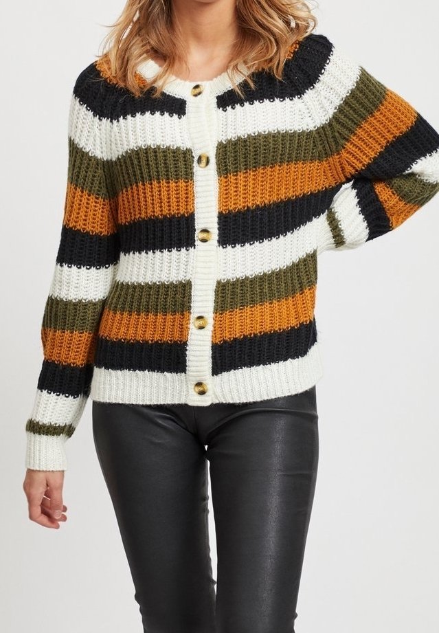Femme portant un cardigan en maille côtelée boutonné avec des rayures horizontales en blanc, noir, vert olive et orange, associé à un pantalon en cuir noir.