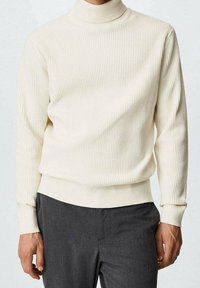 Cremfarbener Rollkragenpullover mit horizontaler Rippstruktur, taillierter Passform und langen Ärmeln, kombiniert mit grauen Hosen.