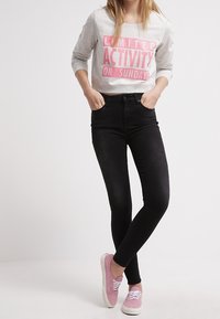 Šedá dlouhá košile s růžovým textem, černé úzké džíny a růžové semišové tenisky s bílou podrážkou a tkaničkami. Neformální outfit.