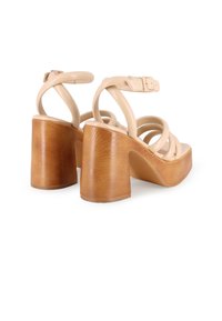 Sandalias de tacón alto de cuero beige con un chunky de madera, que presentan múltiples tiras entrelazadas y una hebilla en el tobillo ajustable.