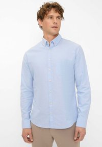 Hellblaues langärmliges Hemd mit Knopfleiste, kragen, vorderer Tasche und leichter Stoffstruktur. Gerader Saum und Knopfdetails vorhanden.