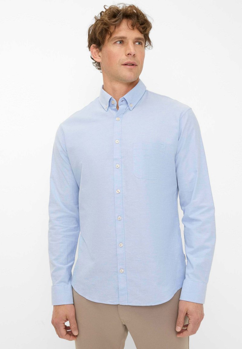 Hellblaues langärmliges Hemd mit Knopfleiste, kragen, vorderer Tasche und leichter Stoffstruktur. Gerader Saum und Knopfdetails vorhanden.
