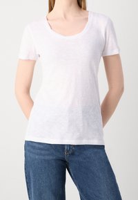 Hvid kortærmet T-shirt med bådudskæring, lavet af et letvægts, let struktureret stof, parret med blå denim jeans.