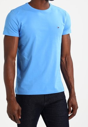 T-shirt azzurro chiaro a maniche corte realizzato in tessuto morbido, con scollatura a girocollo e piccolo logo sul petto. Indossato con jeans scuri.