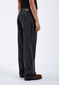 High-waisted, loose black denim jeans with a straight leg fit. Features a back patch pocket and allows for comfort and mobility.