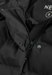 Schwarze Pufferjacke mit einem Frontreißverschluss, Druckknöpfen und gestepptem Innenfutter. Der Stoff ist glatt mit matter Oberfläche. Innenetikett sichtbar.
