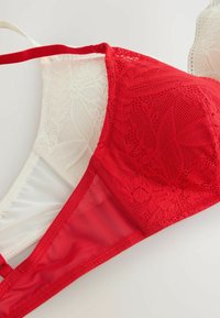 Czerwony koronkowy biustonosz w kształcie trójkąta z przezroczystą białą siateczką. Detale obejmują kwiatowe wzory na koronce oraz regulowane ramiączka. Gładka tekstura całości.