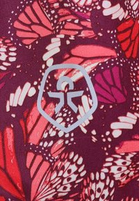 Textilie s fialovým pozadím s živými vzory motýlů v růžové a bílé barvě. Šedé logo uprostřed připomíná ikonu osoby v štítu.