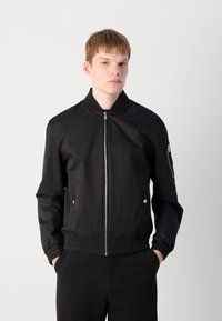 Black bomber jacket with a zip front, knit collar, two front pockets, ribbed cuffs, and a side zip pocket. Smooth, matte fabric.