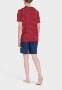 Camicetta rossa a maniche corte con pois blu, pantaloni corti blu navy. Tessuto comodo, colletto con rifinitura a contrasto, design semplice, senza loghi visibili.