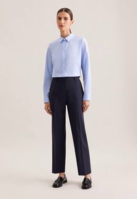 Lichtblauw cropped overhemd met knopen, marineblauwe getailleerde broek en zwarte loafers. Soepele stof, klassieke kraag, gevormde pasvorm.