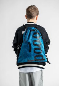 Zaino con cordoncino in tessuto tie-dye blu, caratterizzato da un grande logo nero, con spallacci regolabili e chiusura a sacco.