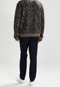 Maglione da uomo grigio scuro con un motivo astratto nero, abbinato a pantaloni blu navy e sneaker bianche. Il maglione presenta polsini e orlo a costine.